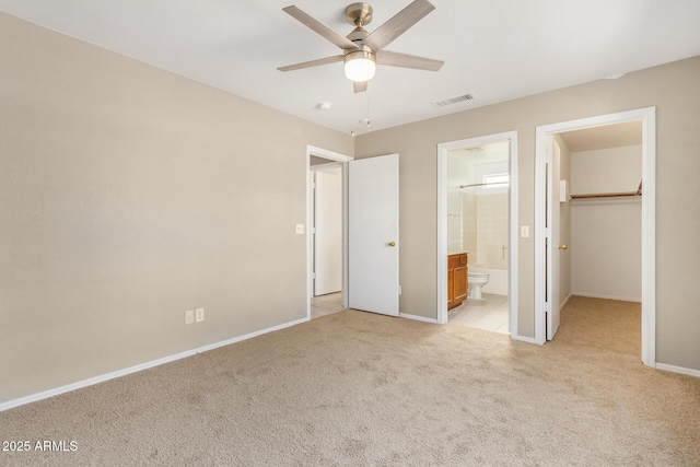 unfurnished bedroom with connected bathroom, a spacious closet, light colored carpet, ceiling fan, and a closet