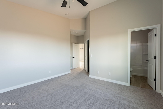 unfurnished bedroom featuring carpet floors, ensuite bathroom, a ceiling fan, high vaulted ceiling, and baseboards