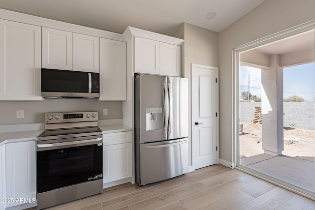 kitchen with light wood finished floors, white cabinetry, appliances with stainless steel finishes, and light countertops