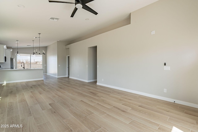 unfurnished living room with ceiling fan with notable chandelier, light wood finished floors, a sink, and visible vents