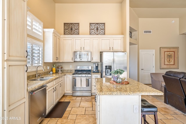 kitchen with a center island, appliances with stainless steel finishes, sink, and a towering ceiling