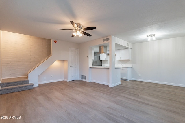 unfurnished living room featuring ceiling fan, a textured ceiling, and light wood-type flooring