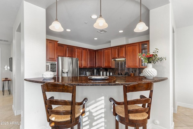 kitchen with appliances with stainless steel finishes, hanging light fixtures, backsplash, a kitchen bar, and kitchen peninsula