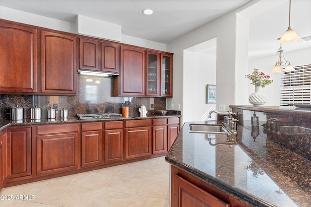 kitchen featuring stainless steel gas cooktop, sink, hanging light fixtures, dark stone counters, and backsplash