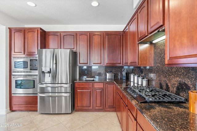 kitchen with appliances with stainless steel finishes, light tile patterned floors, decorative backsplash, and dark stone counters