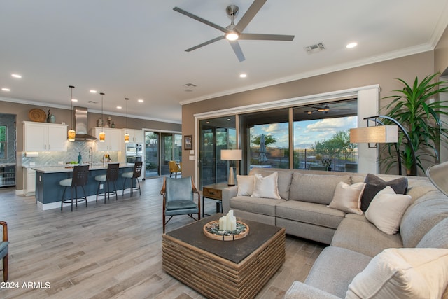 living room with light hardwood / wood-style flooring, sink, crown molding, and ceiling fan