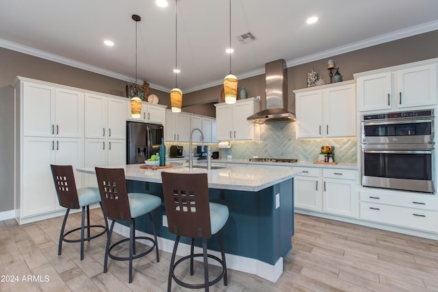 kitchen featuring wall chimney exhaust hood, appliances with stainless steel finishes, hanging light fixtures, and white cabinets