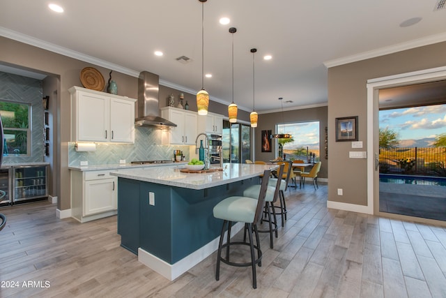 kitchen featuring wall chimney exhaust hood, pendant lighting, a center island with sink, and white cabinets