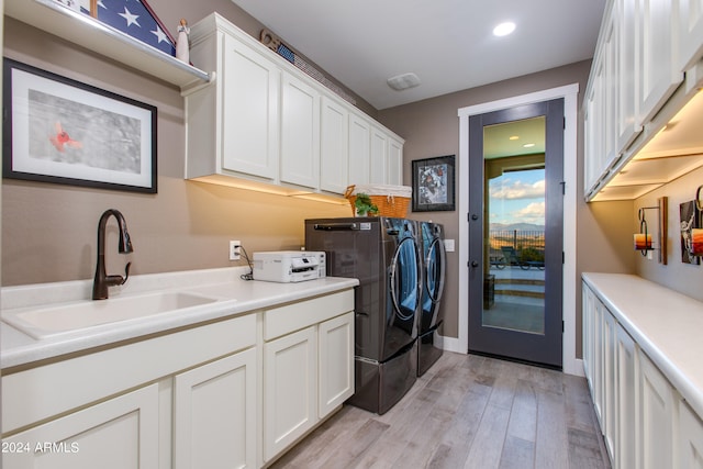 clothes washing area featuring light hardwood / wood-style floors, sink, cabinets, and washing machine and dryer