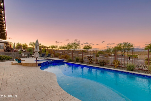 pool at dusk featuring a patio and an in ground hot tub