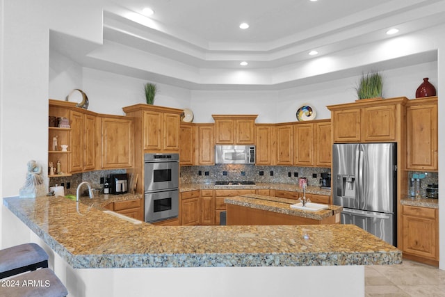 kitchen featuring appliances with stainless steel finishes, a towering ceiling, a kitchen breakfast bar, tasteful backsplash, and kitchen peninsula