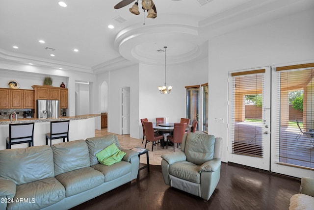 living room with dark hardwood / wood-style flooring, a towering ceiling, ceiling fan with notable chandelier, and a tray ceiling