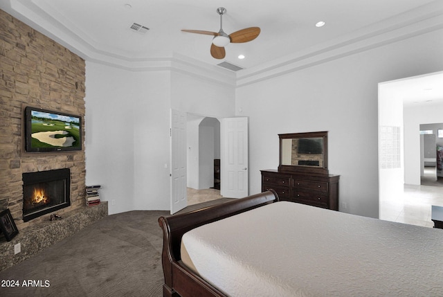 carpeted bedroom with ceiling fan, a stone fireplace, and a high ceiling