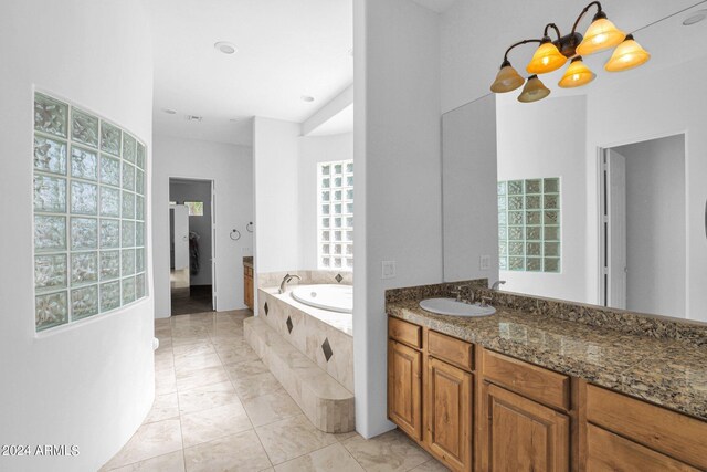 bathroom with a notable chandelier, vanity, tile patterned flooring, and tiled tub