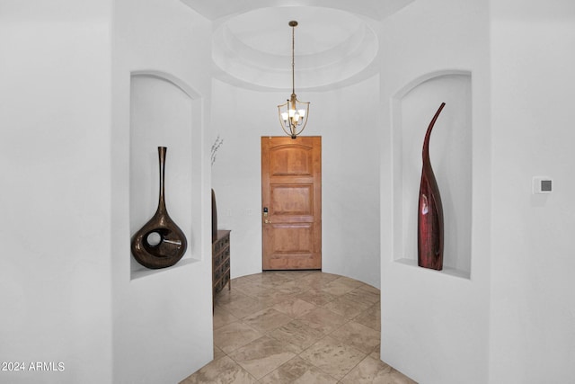 hallway featuring an inviting chandelier and a tray ceiling