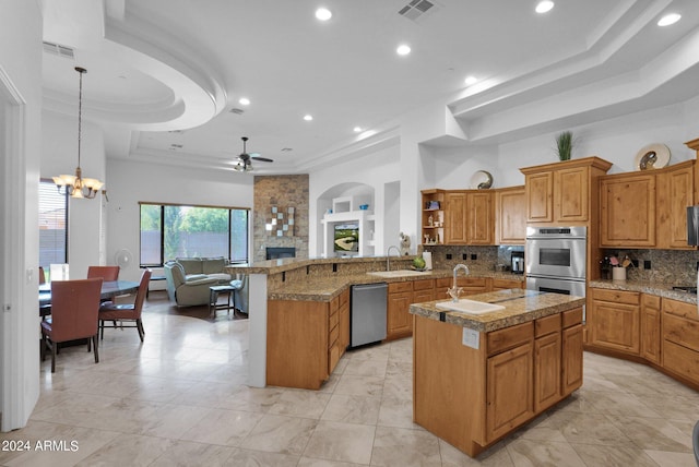 kitchen with pendant lighting, sink, appliances with stainless steel finishes, a kitchen island with sink, and kitchen peninsula