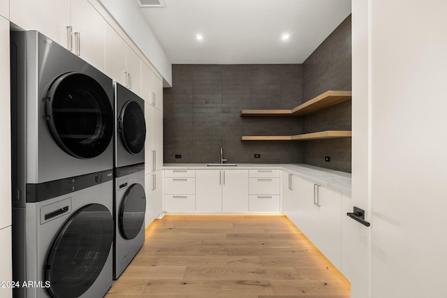 laundry area with light wood-type flooring, cabinets, sink, and stacked washer and dryer