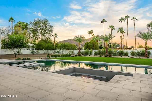 pool at dusk featuring a mountain view, a patio, and a yard