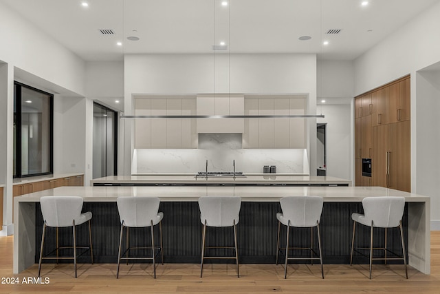 kitchen with a kitchen breakfast bar, light hardwood / wood-style floors, white cabinetry, and a large island with sink