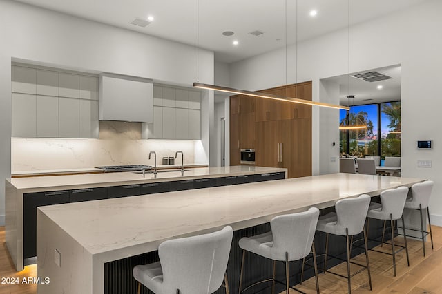 kitchen with a spacious island, light hardwood / wood-style floors, white cabinets, and decorative light fixtures