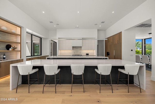 kitchen featuring a spacious island, light wood-type flooring, a breakfast bar, and white cabinets