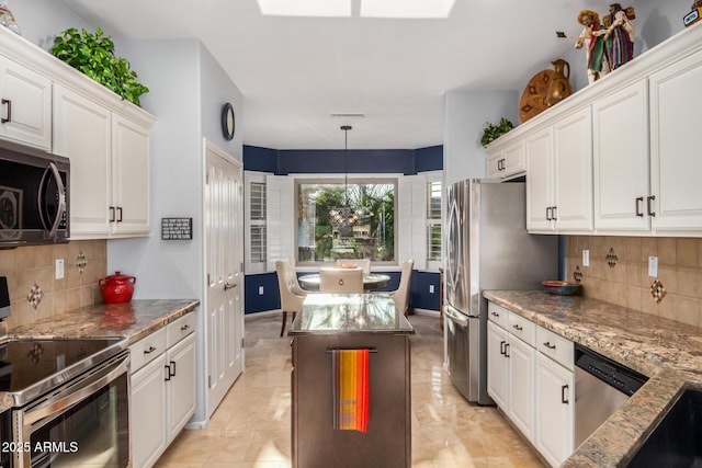 kitchen with white cabinets, hanging light fixtures, appliances with stainless steel finishes, light stone countertops, and tasteful backsplash