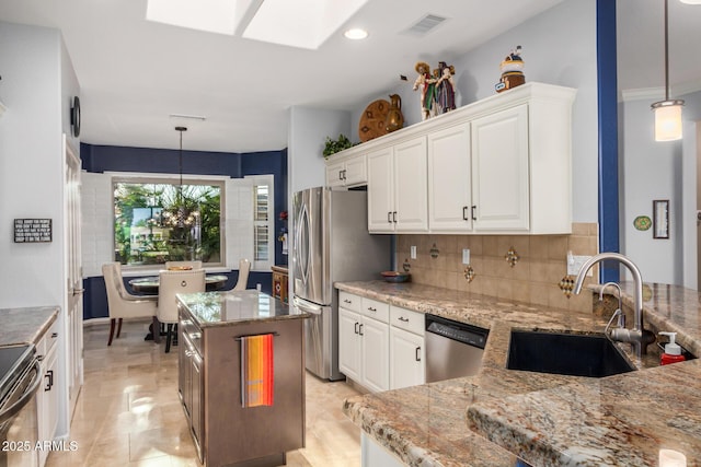 kitchen with a kitchen island, appliances with stainless steel finishes, light stone countertops, white cabinetry, and a sink