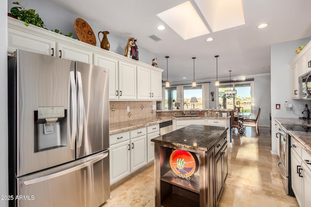 kitchen featuring a peninsula, appliances with stainless steel finishes, decorative light fixtures, and white cabinets