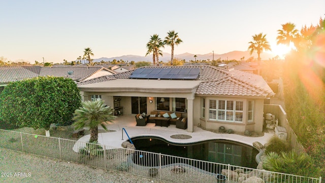 back of property with solar panels, a fenced backyard, a tiled roof, a mountain view, and an outdoor living space