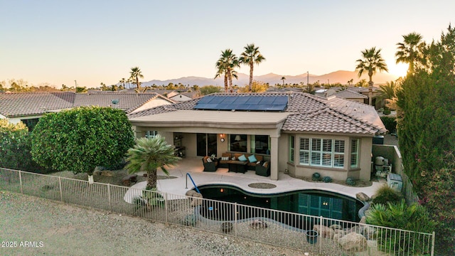 rear view of property featuring a fenced backyard, an outdoor hangout area, solar panels, a tile roof, and a patio area