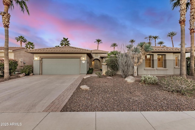 view of front of home with concrete driveway, an attached garage, a tiled roof, and stucco siding