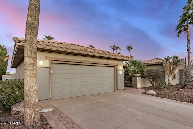 mediterranean / spanish-style house with a garage, driveway, a tile roof, and stucco siding