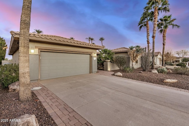 mediterranean / spanish home with driveway, a tiled roof, an attached garage, and stucco siding