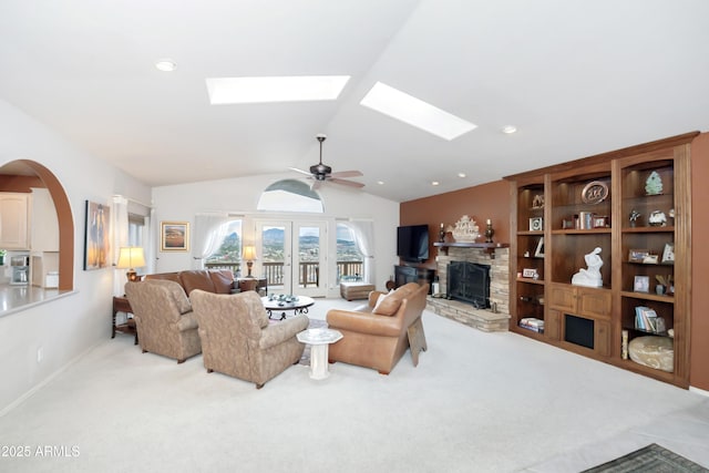 living area with lofted ceiling with skylight, ceiling fan, a stone fireplace, and light colored carpet