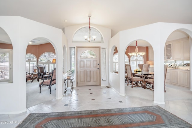 entrance foyer featuring a chandelier, light tile patterned flooring, light colored carpet, baseboards, and vaulted ceiling