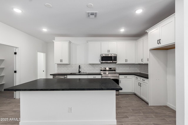 kitchen featuring stainless steel appliances, wood finish floors, a sink, visible vents, and dark countertops