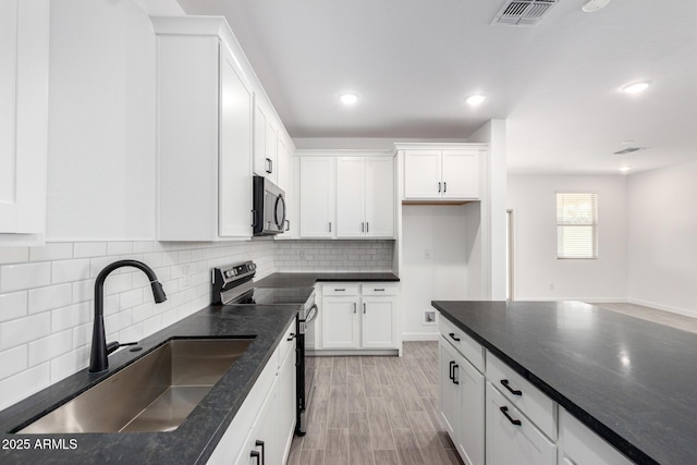 kitchen featuring visible vents, decorative backsplash, white cabinets, appliances with stainless steel finishes, and a sink