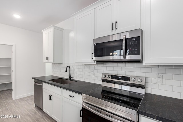 kitchen featuring stainless steel appliances, a sink, white cabinetry, baseboards, and backsplash