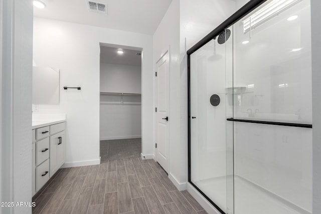 bathroom featuring visible vents, a spacious closet, a stall shower, vanity, and baseboards