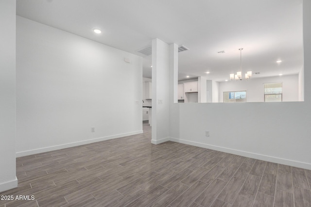 unfurnished living room with a chandelier, wood finished floors, visible vents, and baseboards