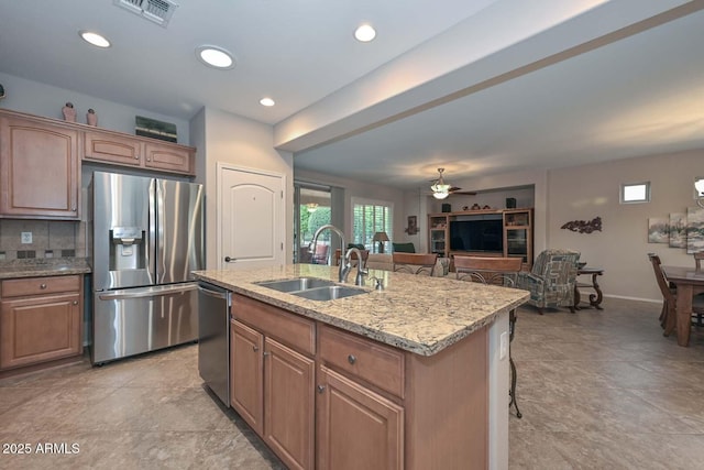 kitchen with sink, a kitchen bar, a kitchen island with sink, light stone counters, and stainless steel appliances