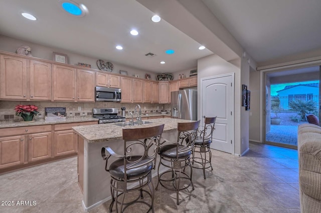 kitchen featuring an island with sink, sink, decorative backsplash, stainless steel appliances, and light stone countertops