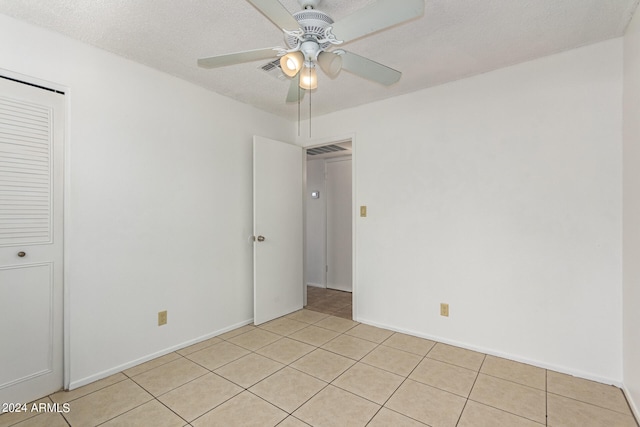 spare room featuring ceiling fan, light tile patterned floors, and a textured ceiling