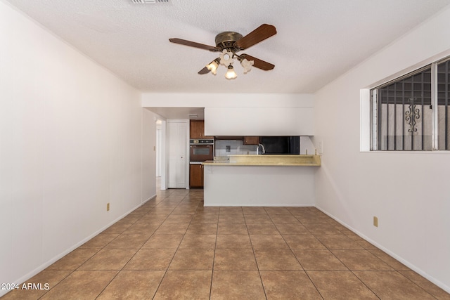 kitchen with a textured ceiling, kitchen peninsula, stainless steel oven, tile patterned floors, and ceiling fan