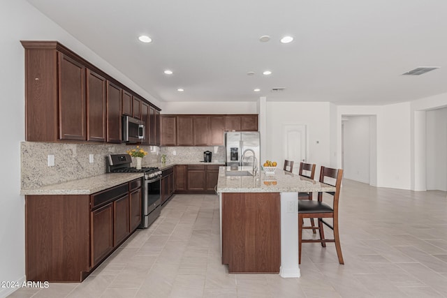 kitchen with light stone counters, tasteful backsplash, a breakfast bar area, stainless steel appliances, and a center island with sink