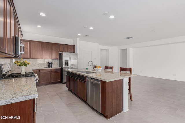 kitchen with a kitchen island with sink, sink, a kitchen bar, stainless steel appliances, and backsplash