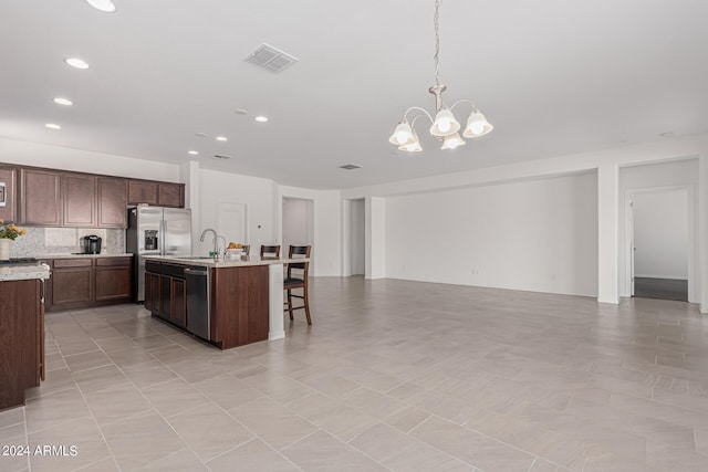 kitchen featuring appliances with stainless steel finishes, light tile patterned floors, decorative light fixtures, a kitchen island with sink, and a notable chandelier