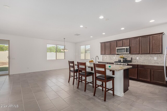 kitchen featuring a center island with sink, appliances with stainless steel finishes, a breakfast bar, and a healthy amount of sunlight