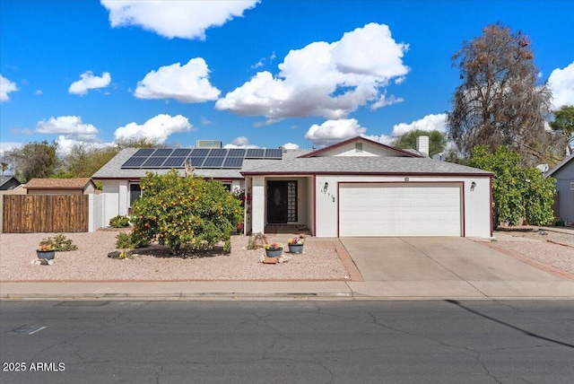 ranch-style home featuring a garage, fence, concrete driveway, roof mounted solar panels, and stucco siding