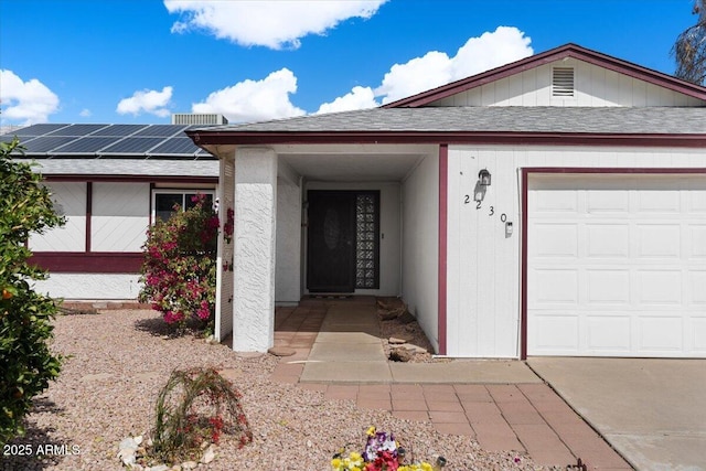 ranch-style house featuring an attached garage, a shingled roof, and solar panels